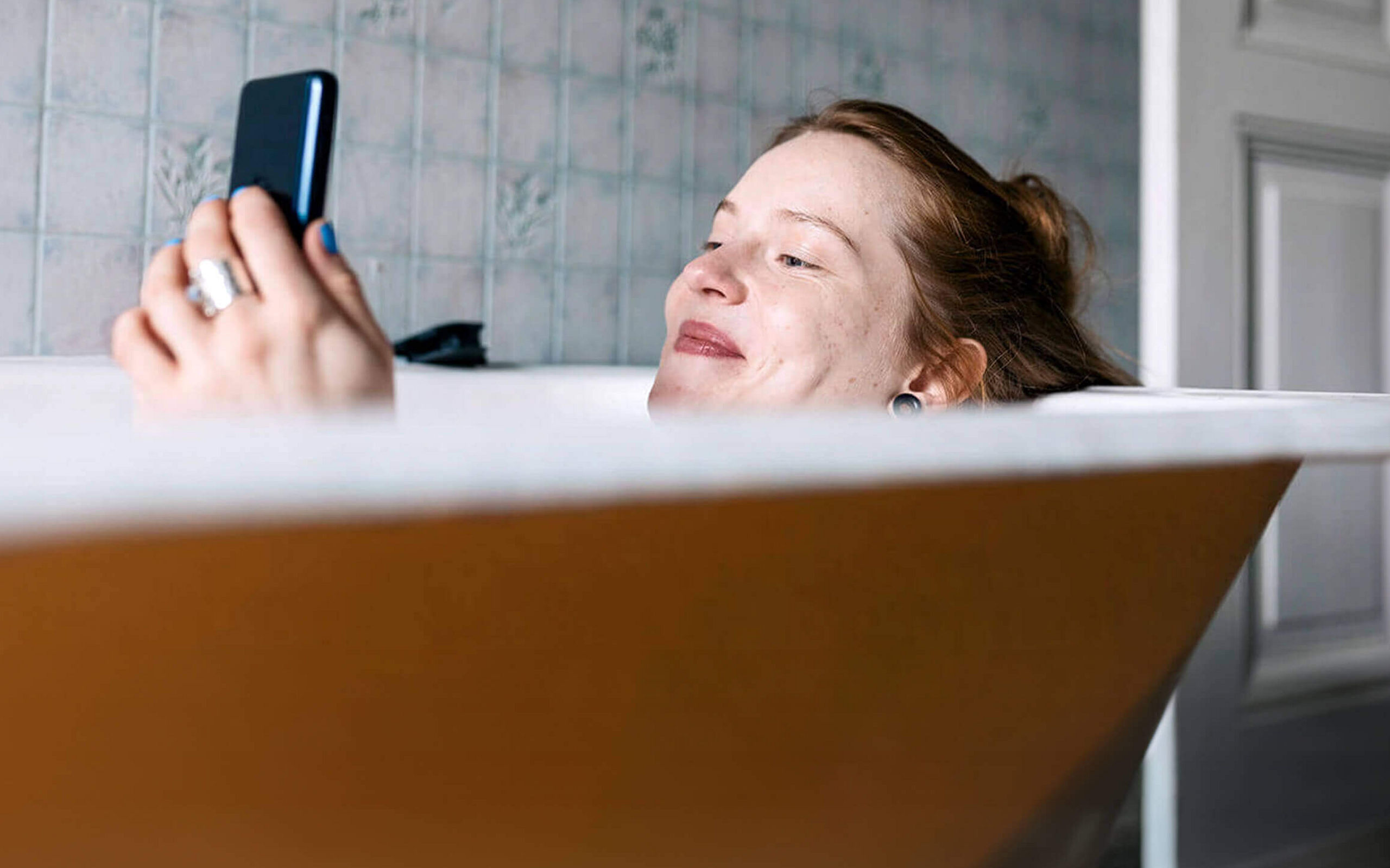 Eine Frau liegt in der Badewanne und schaut auf ihr Smartphone