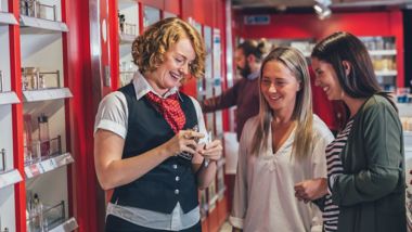 Smiling friends testing perfume with staff member in shop